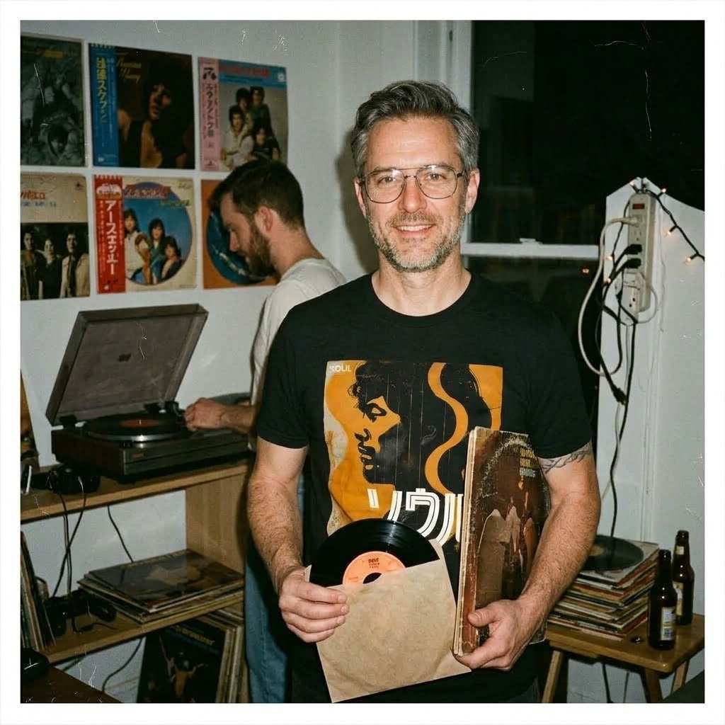 Man i vintage-inspirerad rumsmiljö med vinylskivor och Nippon Grooves t-shirt i svart. Acceso.se