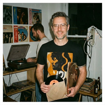 Man i vintage-inspirerad rumsmiljö med vinylskivor och Nippon Grooves t-shirt i svart. Acceso.se